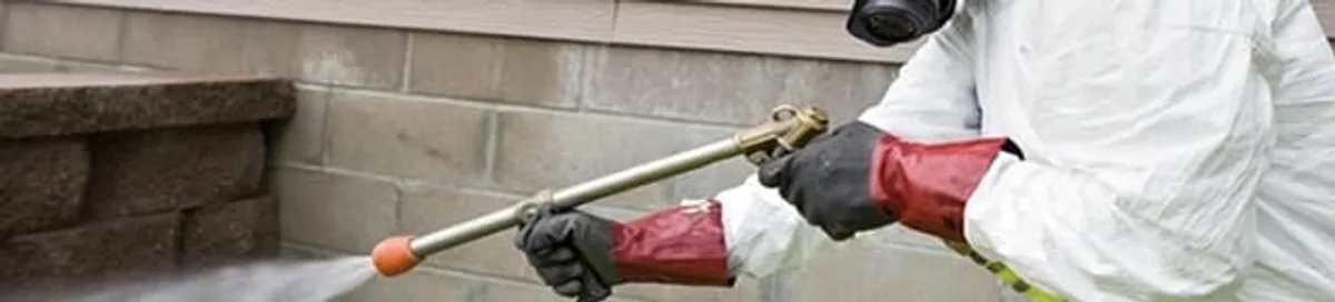 Pest control technician applying exterior insect treatment along a home foundation in Marietta, GA