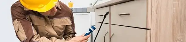 Roach exterminator applying treatment under kitchen cabinets in Marietta, GA