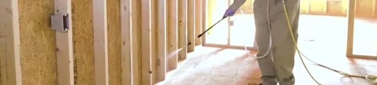 Termite treatment technician applying spray along framing and unfinished walls in Marietta, GA