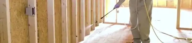 Termite treatment technician applying spray along framing and unfinished walls in Marietta, GA